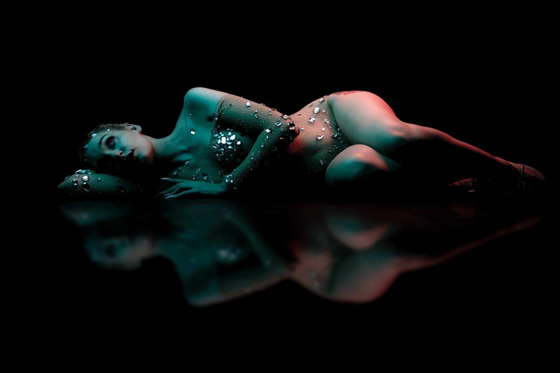 young woman lying on the floor wearing a sheer sparkling nylon bodysuit for an high contrast boudoir photo session