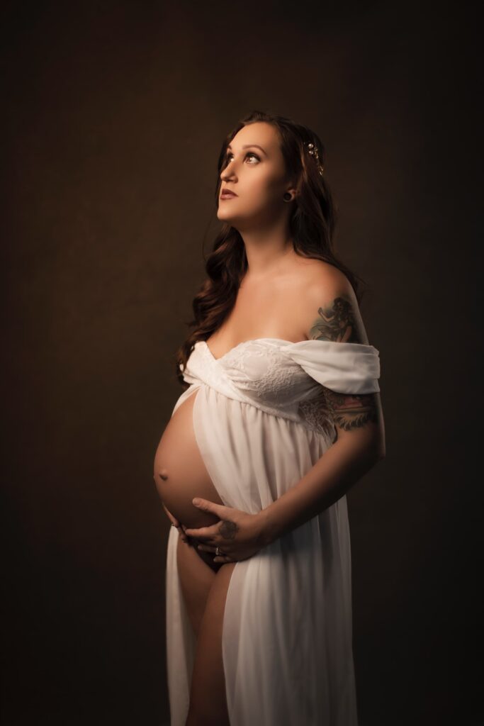 a pregnant inked model if posing in the nude wearing a long open night gown showing her belly