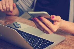 woman hand with nail polish hold a mobile phone on top of a laptop