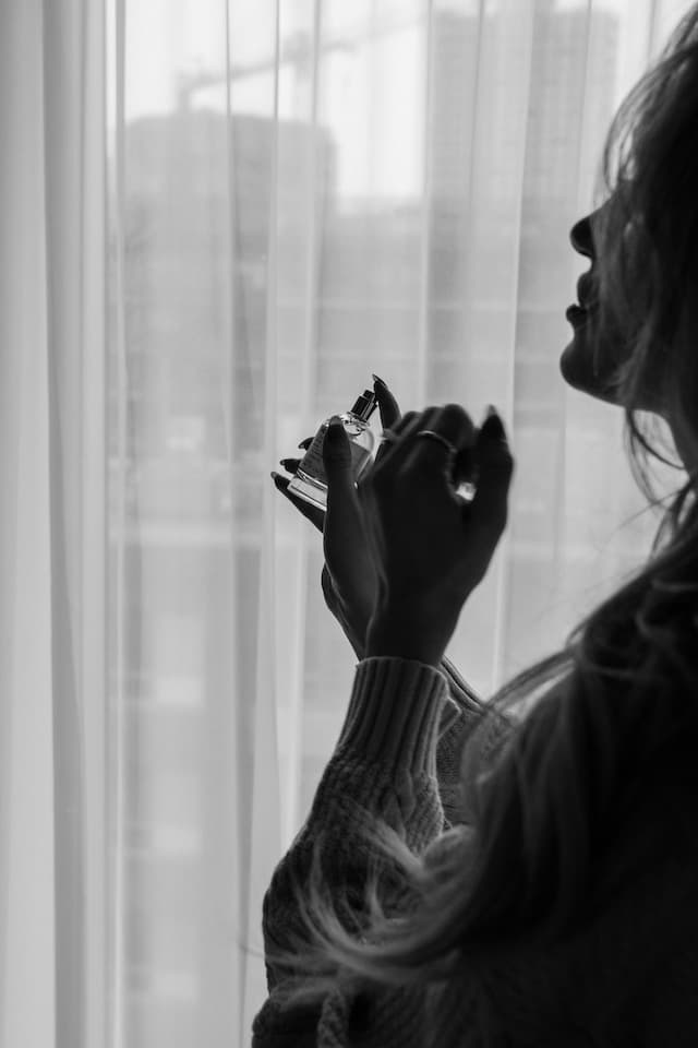 black and white picture of a woman holding perfume in front of a window