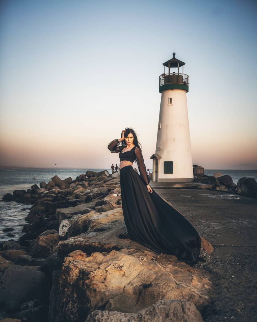 Beautiful woman posing in front of a lighthouse with rocks and sea at blue hour. Photo by Rita Hough