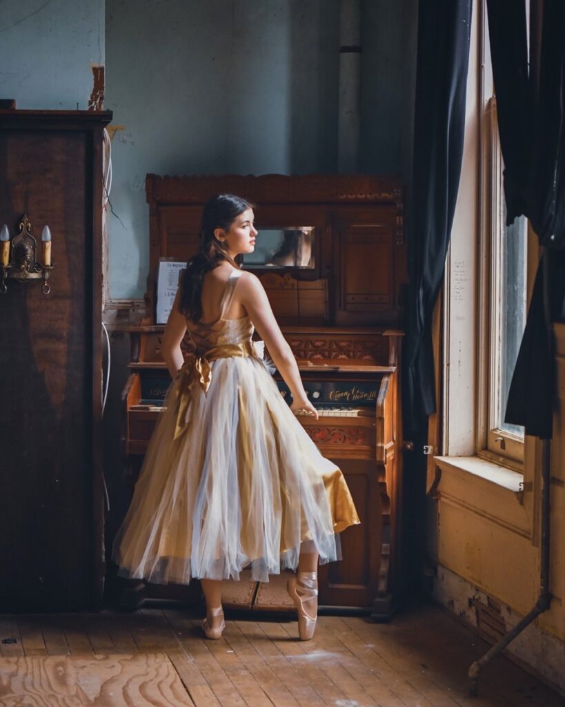 Young ballerina standing in front of a old wooden organ. Photo by Rita Hough