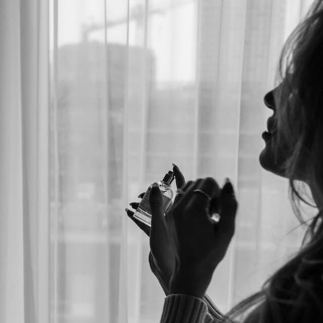 black and white picture of a woman holding perfume in front of a window