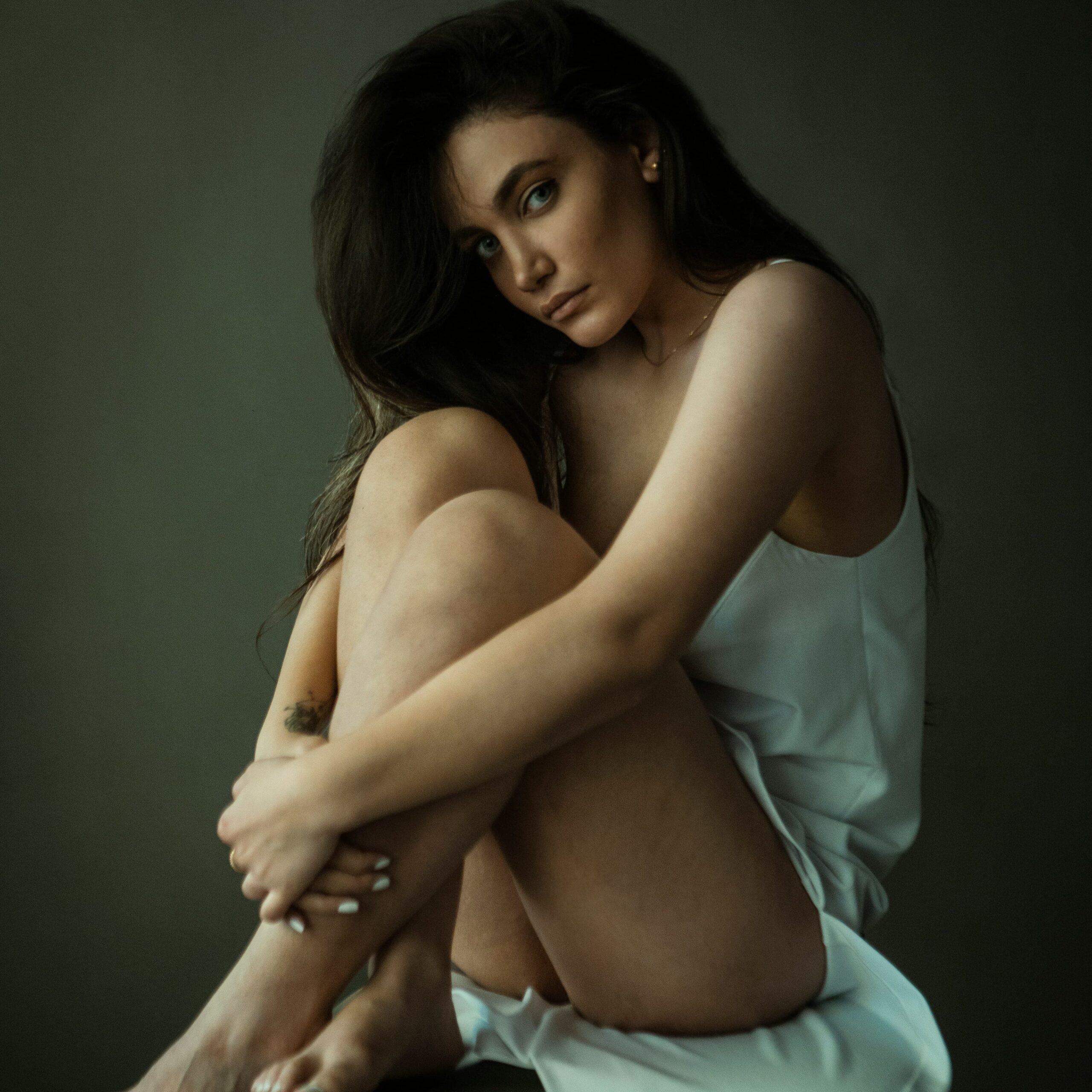 beautiful woman sitting barefoot holding her legs wearing a light summer dress